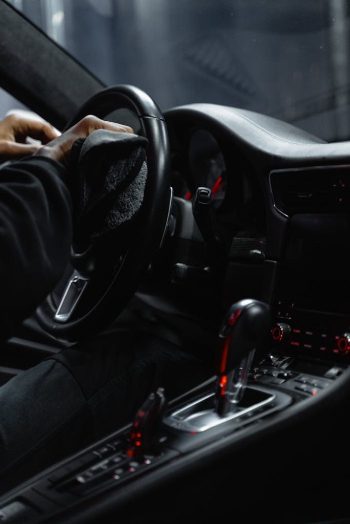 Close-up of a person cleaning a cars dashboard and steering wheel, focused on interior maintenance.